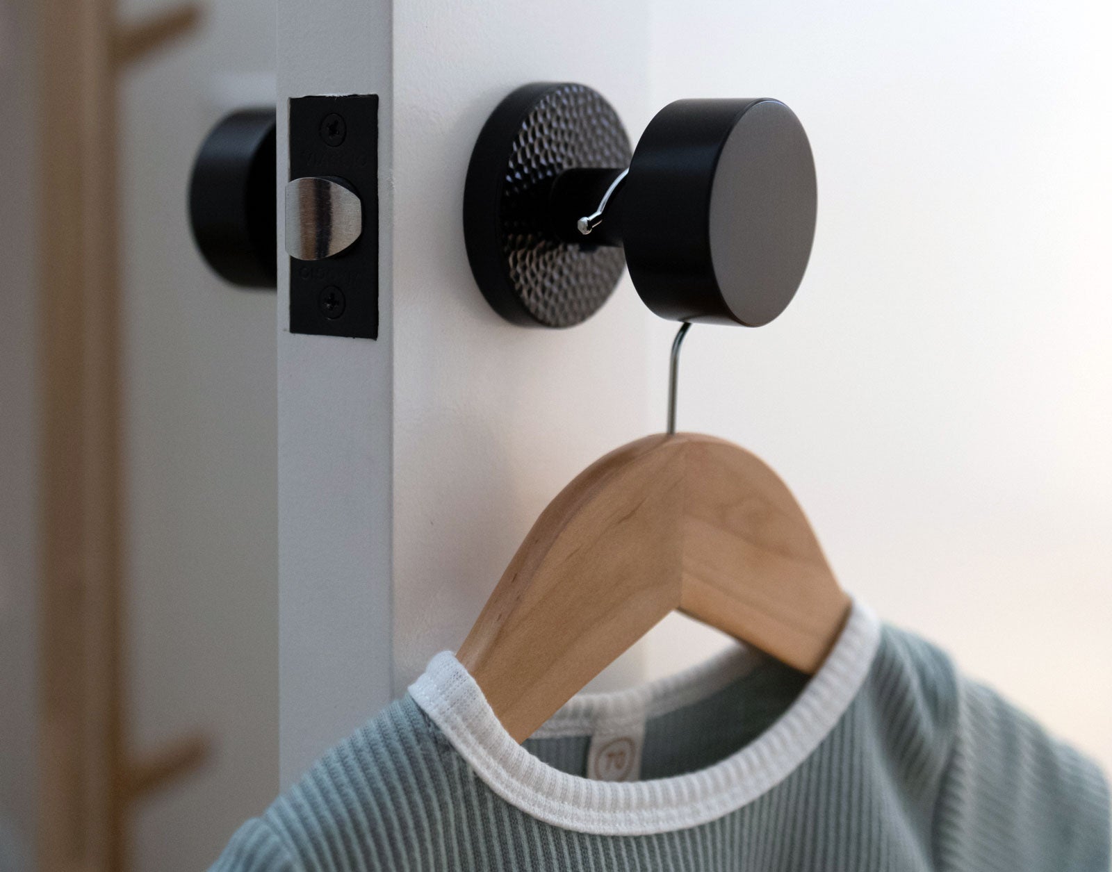 white closet door with black modern hardware with clothes hanger and baby clothes