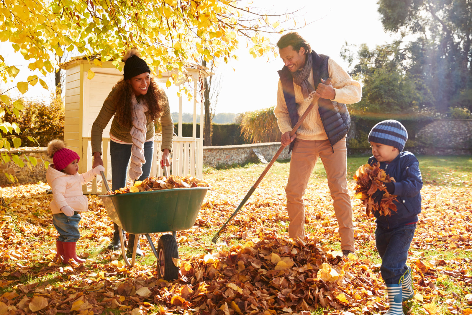 family raking leaves together in the fall with a wheelbarrow