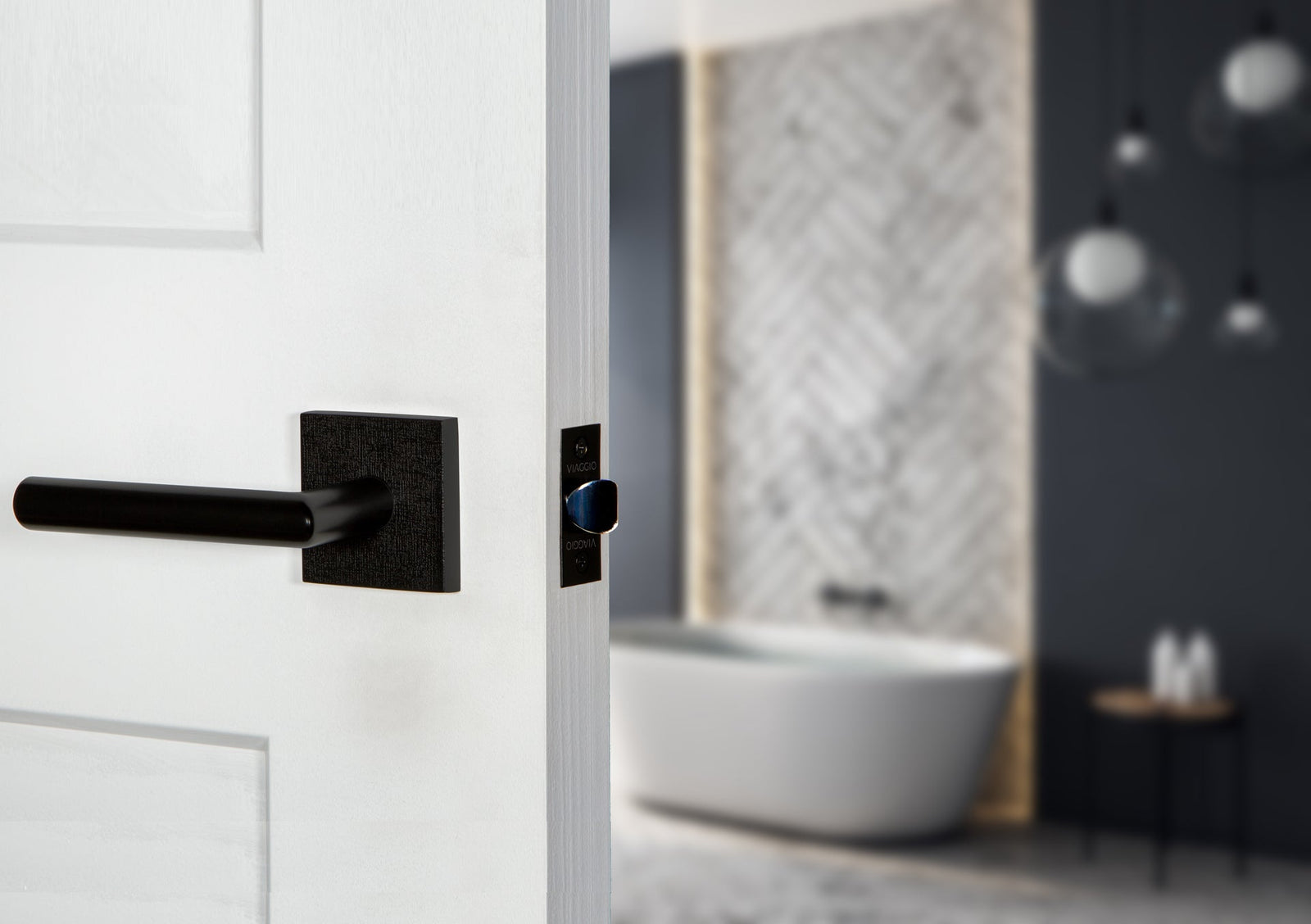 contemporary bathroom with navy blue walls and chevron herringbone wall tile with a white door and black lever square hardware from viaggio